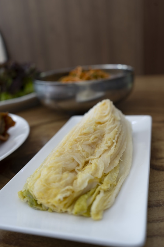 흰 긴 접시에 담은 백김치, 뒤에 파채 그릇과 쌈채소